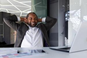 bem feito homem de negocios com sucesso concluído a trabalhar, descansos dentro a escritório sonhadoramente e pensativo, a homem lança dele mãos atrás dele cabeça e visualiza a futuro vitórias e conquista. foto