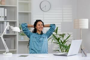 jovem empresária com olhos fechadas inclinado costas dentro dela cadeira, levando uma relaxante pausa às dela local de trabalho dentro uma brilhante escritório. foto