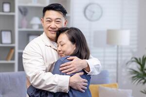 feliz ásia casal homem e mulher juntos às casa sorridente e abraçando, família dentro vivo sala. foto