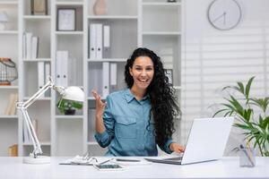 uma alegre hispânico empresária é visto trabalhando a partir de lar, expressando positividade e sucesso enquanto olhando às a Câmera. foto