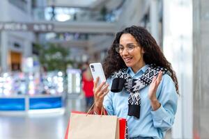 feliz fêmea comprador dentro loja falando em ligar com amigos, hispânico mulher usando Smartphone para conectados controlo remoto comunicação, partilha em formação sobre vendas e descontos foto