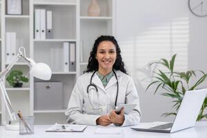 confiante fêmea médico com uma estetoscópio por aí dela pescoço, sorridente calorosamente dentro uma bem iluminado, moderno médico escritório, exalando profissionalismo e Cuidado. foto