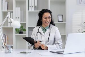 uma alegre hispânico médico envolve dentro uma chamar, sugerindo uma virtual consulta, dentro uma brilhante médico escritório contexto. foto