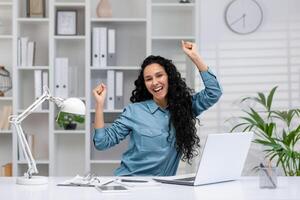 uma alegre hispânico mulher trabalhando a partir de casa comemora uma vitória ou Boa notícias, mostrando positividade e confiança. foto