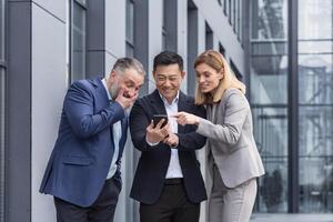 diverso o negócio grupo, três masculino e fêmea trabalhadores lado de fora escritório construção alegremente sorridente e feliz assistindo em telefone foto