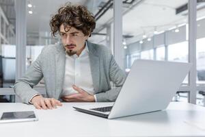 adulto homem de negocios sentindo-me indisposto às dele local de trabalho dentro uma moderno escritório, exibindo típica escritório trabalhos atributos e indicando estresse. foto