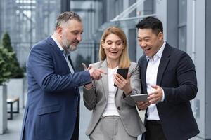 três isto especialistas empreendedores lado de fora escritório construção assistindo em do colega telefone, feliz e sorridente em repouso em pausa a partir de trabalhos foto