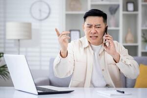 Bravo Bravo e chateado homem falando em telefone às lar, ásia trabalhando remotamente a partir de casa escritório sentado às mesa dentro vivo sala, freelance homem de negocios às trabalhar. foto