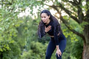 retrato do uma lindo fêmea atleta dentro a parque, hispânico mulher descansos e respira durante corrida e ativo fisica exercício, fêmea atleta dentro roupa de esporte tem peito dor. foto