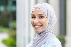 uma retrato do uma alegre mulher vestindo uma hijab, irradiando confiança e contentamento com uma borrado fundo. foto