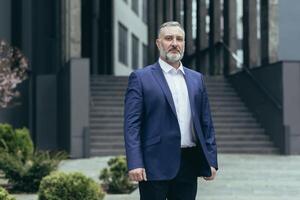 governo representante. retrato do uma Senior homem dentro uma o negócio terno, deputado, senador. ele é em pé sério perto a moderno governo prédio, olhando para dentro a Câmera foto