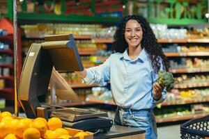 retrato do uma feliz comprador dentro uma supermercado dentro a fruta e vegetal seção, hispânico mulher pesagem repolho sorridente e olhando às a Câmera foto