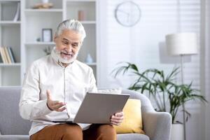 idosos masculino usando uma computador dentro uma brilhante, contemporâneo vivo sala, ficando conectado e produtivo às lar. foto