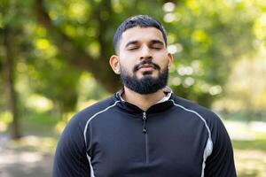 uma sereno homem praticando atenção meditação ao ar livre, olhos fechadas e cercado de exuberante vegetação dentro uma tranquilo parque ambiente. foto