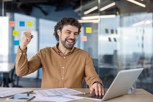 a muito feliz homem de negocios levantando dele punho dentro triunfo às uma bem iluminado ambiente de trabalho, exalando confiança e sucesso. foto