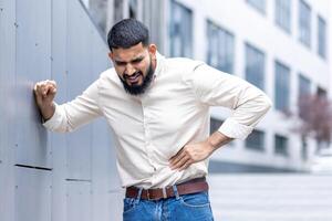 jovem homem expressando desconforto com uma dor de estômago ao ar livre foto
