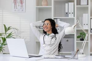 uma latino fêmea médico leva uma momento para relaxar às dela escrivaninha dentro uma bem iluminado, moderno médico escritório, exalando uma sentido do calma e profissionalismo. foto