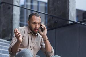 depressivo homem sentado em escadas do escritório prédio, frustrado falando em telefone, chateado e disparamos escritório trabalhador fechar acima dentro casual camisa foto