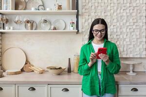 lindo mulher dentro óculos e verde camisa usando vermelho Móvel telefone às casa foto
