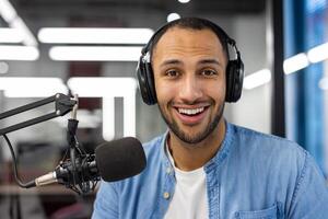 a indiano homem dentro uma jeans camisa hospedeiros uma podcast a partir de dele bem iluminado vivo sala, incorporando uma casual ainda profissional trabalho a partir de casa vibe. foto