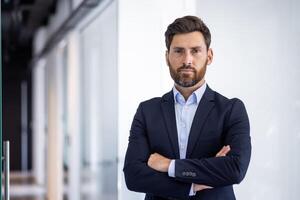 retrato do sério autoconfiante masculino advogado em pé dentro escritório, cruzado braços em peito e olhando às Câmera. foto