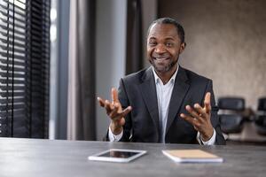 uma homem dentro uma terno é sentado às uma escrivaninha com uma tábua e uma caderno. ele é sorridente e ele é acionado dentro uma conversação foto