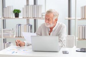 Senior homem verificação seus contas, aposentado idosos velho família lendo documentos, maduro homem dentro vivo quarto com documentos e computador portátil foto