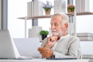 Senior homem verificação seus contas, aposentado idosos velho família lendo documentos, maduro homem dentro vivo quarto com documentos e computador portátil foto