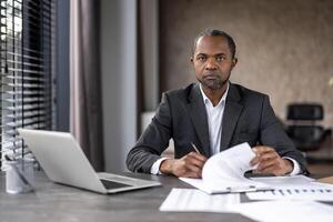 profissional masculino executivo acionado dentro papelada às dele escrivaninha com uma computador portátil dentro a escritório contexto. foto