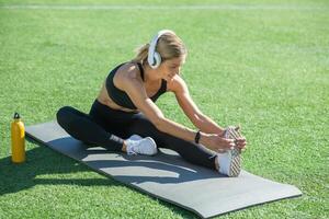uma mulher goza uma ensolarado dia exercício em uma campo com ioga esteira, alongamento antes ginástica rotina foto