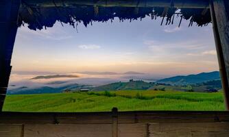 uma Visão do uma campo com uma nebuloso céu e montanhas dentro a fundo. a céu é uma misturar do azul e laranja matizes, criando uma sereno e pacífico atmosfera. arroz terraço Fazenda campo e montanhas. foto