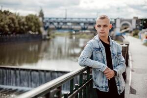 uma jovem homem carrinhos em uma ponte, vestindo uma azul Jaqueta e uma Preto camisa foto