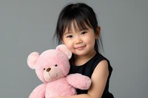 lindo japonês pequeno menina vestindo uma Preto vestir abraçando uma Rosa Urso de pelúcia Urso foto