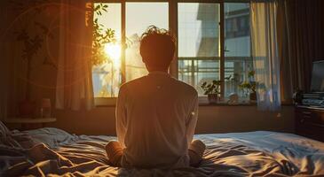 costas Visão do jovem homem meditando em a cama dentro a manhã foto
