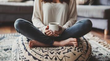 uma pessoa sentado de pernas cruzadas em uma almofada praticando atenção com uma copo do café dentro mão levando dentro cada trago com intenção e gratidão foto