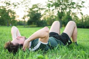 jovem homem com óculos e verde camiseta fazendo abdominais dentro parque foto