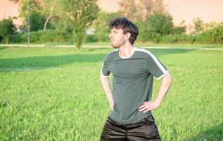 jovem homem com verde camiseta exercício e alongamento dentro parque foto