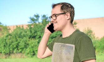 jovem homem com Óculos e verde camiseta falando em célula telefone às a parque foto
