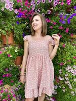 encantador jovem mulher sorridente dentro uma florescendo jardim, cercado de vibrante Rosa e roxa flores, vestindo uma casual Rosa floral vestir foto