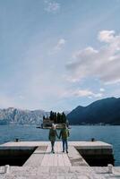 homem e mulher andar segurando mãos ao longo a cais olhando Fora sobre st. George ilha. costas visualizar. Montenegro foto