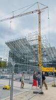 pedestres caminhando perto uma ampla construção local com andaimes e uma imponente amarelo guindaste, Paris, França, abril 14, 2024, representando urbano desenvolvimento foto