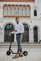 jovem afro-americano usando telefone celular em pé com uma scooter elétrica em uma rua foto