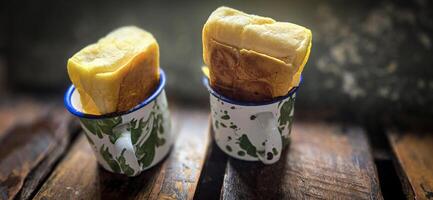 gelo chocolate beber em uma vintage indonésio ferro caneca com aleatória verde padronizar chamado blirik copo ou cangkir blirik em bokeh fundo ao longo com chocolate o preenchimento pão foto