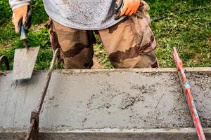 pedreiro espalhando concreto com uma espátula e nível para Construir uma parede às uma construção local foto