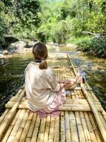 uma menina suavemente flutua baixa uma pequeno rio em uma bambu jangada, imerso dentro a tranquilidade do a em torno da selva panorama foto