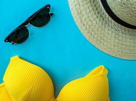 verão período de férias. roupa de banho, oculos de sol e uma chapéu em uma azul fundo foto