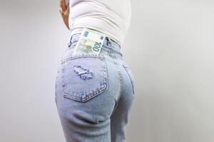 a menina carrinhos costas e tem uma cem euro conta degola Fora do a costas bolso do dela jeans. uma menina dentro jeans com uma euro nota de banco dentro dela mãos. foto