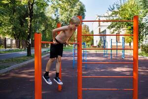 atleta adolescente detém dele mãos em a barra suspensão em isto. rua exercite-se em uma horizontal Barra dentro a escola parque. foto