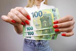 uma fechar-se do uma euro conta com uma denominação do 1 cem que é mantido de uma mulher mãos. uma menina dentro jeans com uma euro nota de banco dentro dela mãos. foto