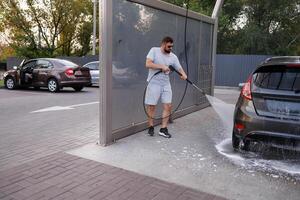 às a carro lavar, uma homem lavagens a espuma espuma fora a inferior do a carro com uma água canhão. uma carro às uma auto serviço carro lavar. foto